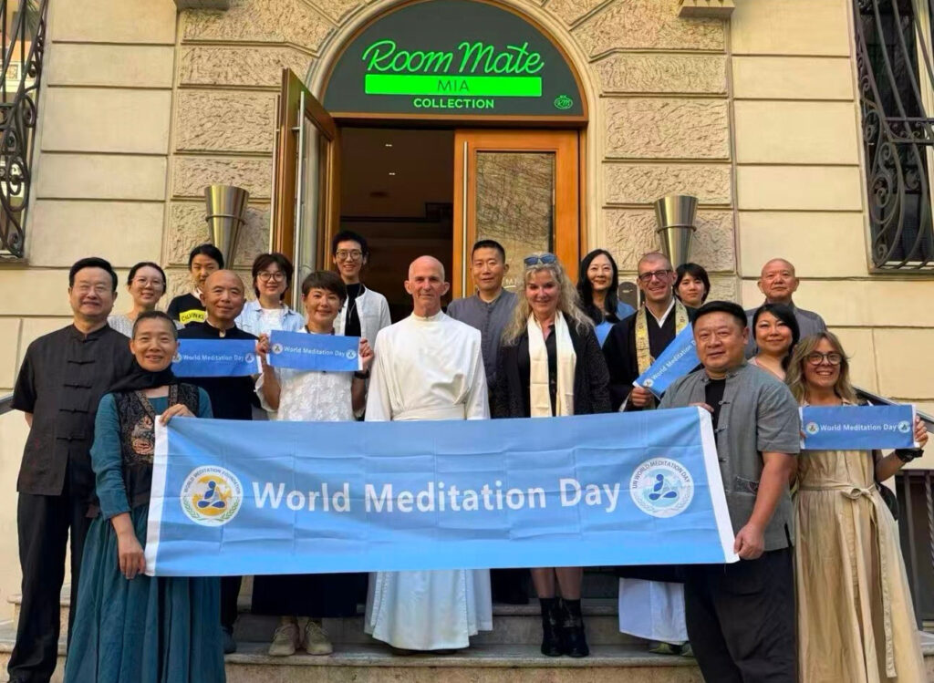 World Meditation Day participants outside a building in Rome, holding a blue event banner.