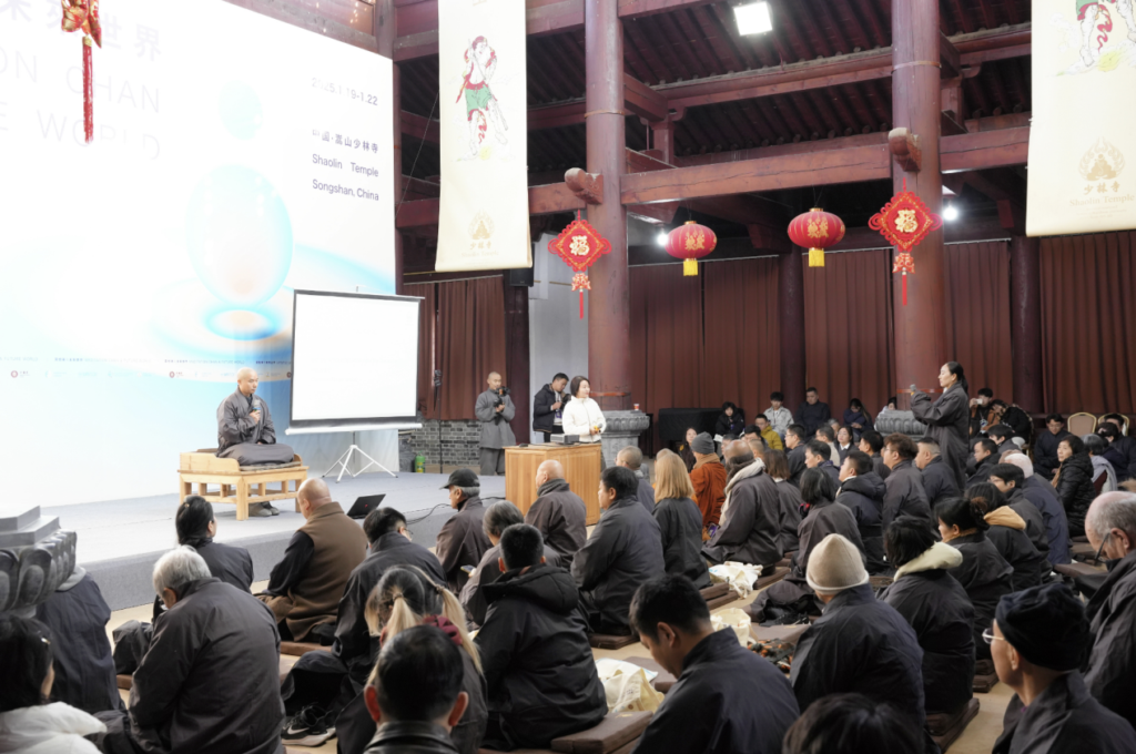 A speaker addresses an audience seated in a temple hall.